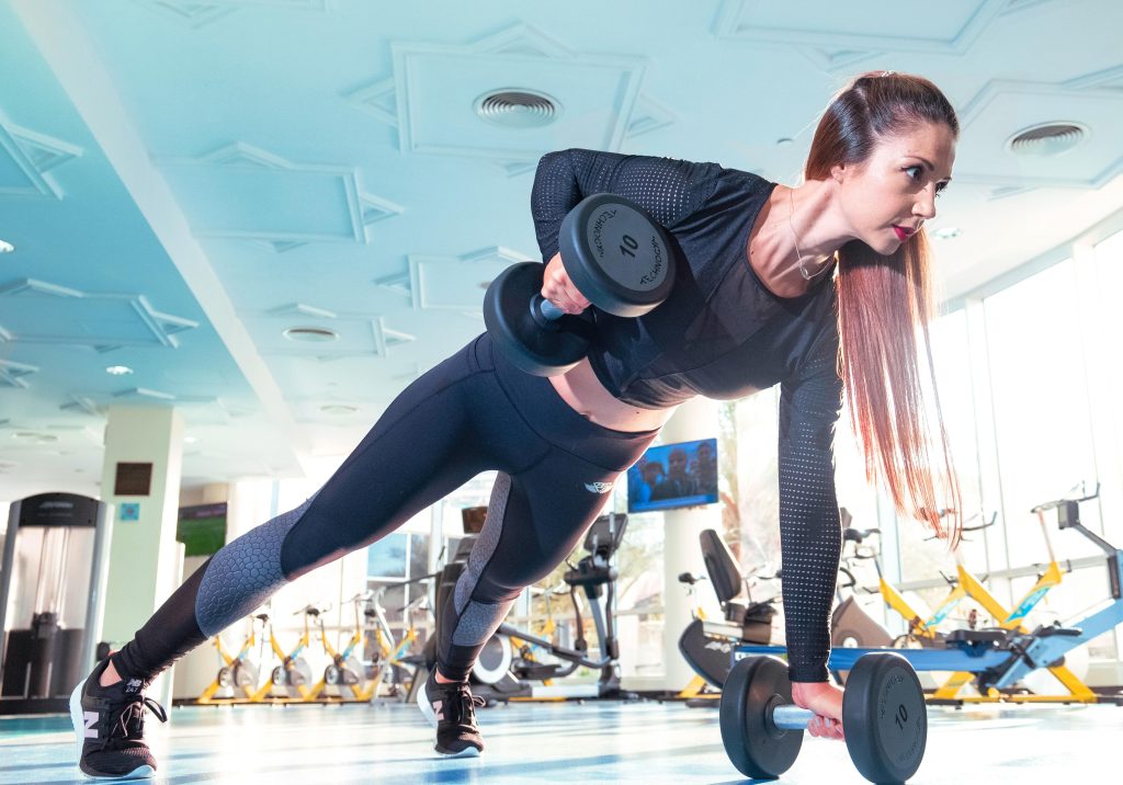 Woman performing a plank row with dumbbells in a bright Dubai gym.