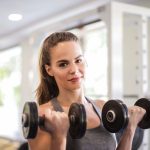 Woman in Gray Tank Top Holding Two Black Dumbbells