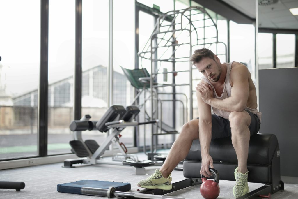 Muscular man in a gym setting, taking a break while holding a kettlebell.