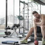 Muscular man in a gym setting, taking a break while holding a kettlebell.