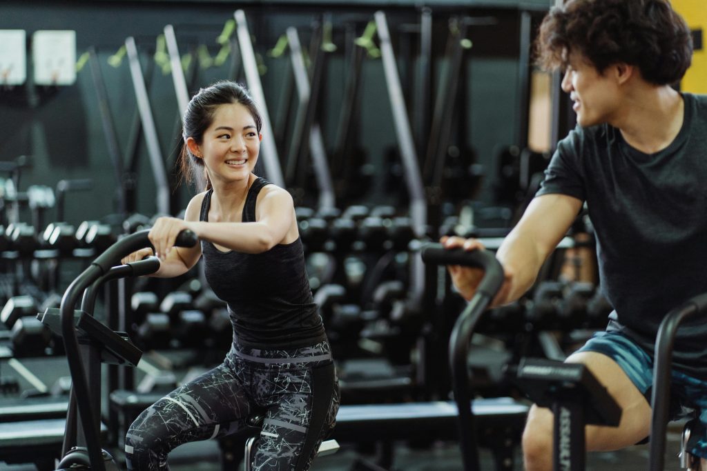 Happy Asian couple working out on elliptical trainers in a gym.