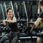 Happy Asian couple working out on elliptical trainers in a gym.