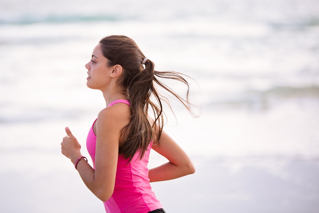 services-01 Side view of a young woman jogging on a beach wearing pink active wear.