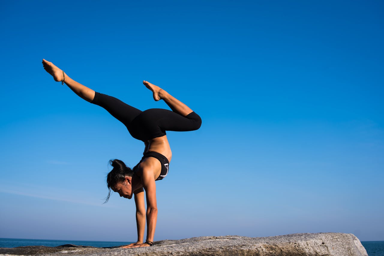 services-03 A woman performing a yoga handstand on a rock by the sea under a clear blue sky.