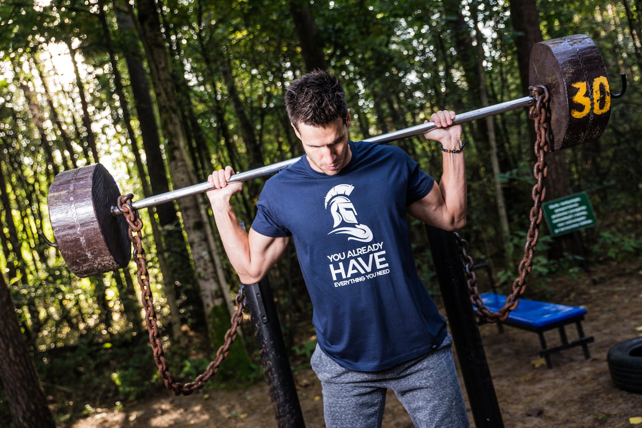 about-07 Man lifting barbell with chains in a wooded outdoor gym, showcasing strength training.