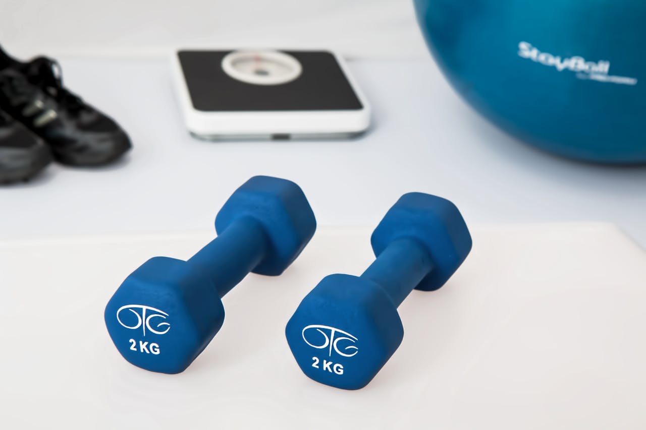 about-01 Blue dumbbells placed on a white surface with fitness equipment in the background.